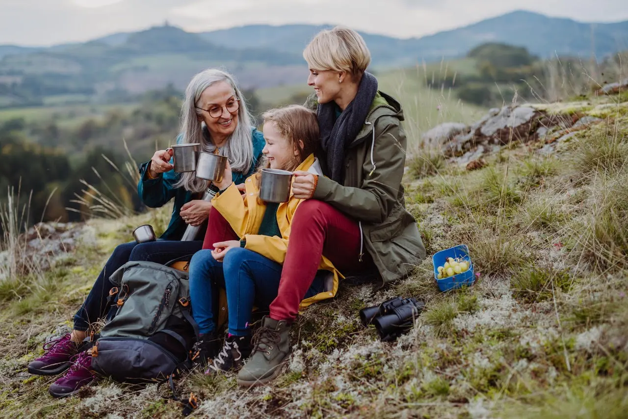 Two older women and a young girl sitting on a grassy hill outside.